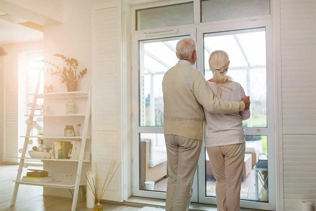 Rearview shot of senior couple looking out living room window Rearview shot of senior couple looking out living room window