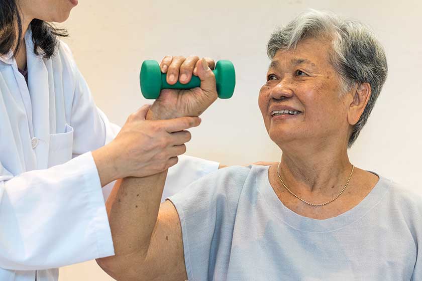 Senior elderly Asia woman with medical caregiver or physical therapist helping patient holding dumbbell Senior elderly Asia woman with medical caregiver or physical therapist helping patient holding dumbbell