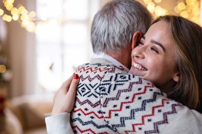 Senior man with young woman indoors at home at Christmas, hugging.