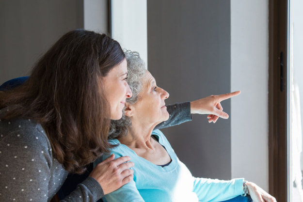Adult daughter visiting elderly mother Adult daughter visiting elderly mother. Young woman showing to senior lady scene out of window. Dementia concept