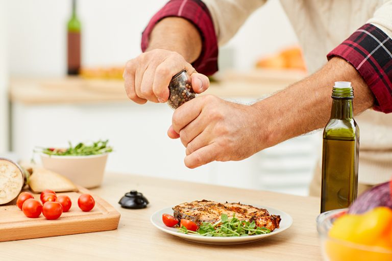 Close up of unrecognizable man sprinkling spices over meat steak while cooking in kitchen