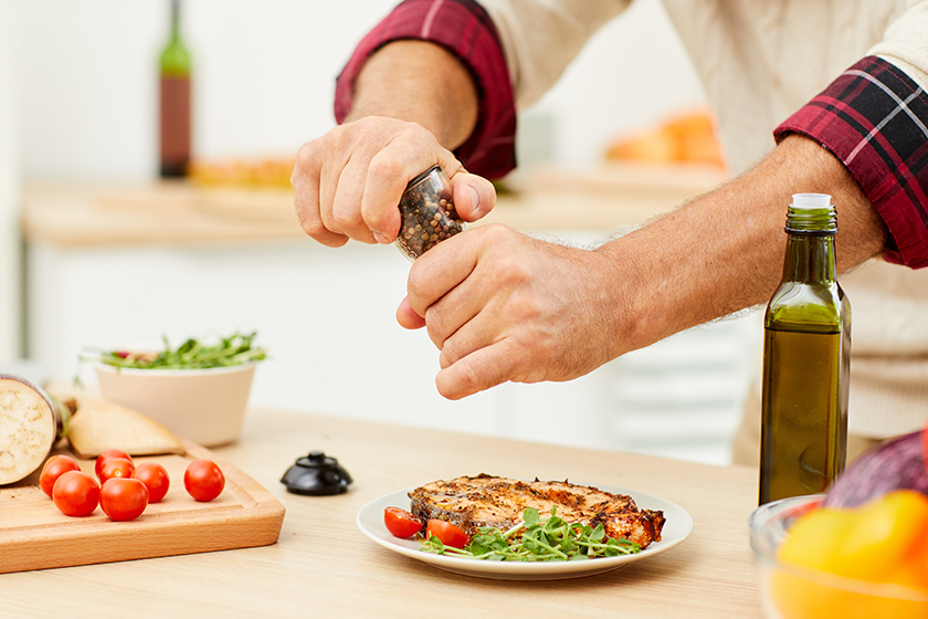 Close up of unrecognizable man sprinkling spices over meat steak while cooking in kitchen
