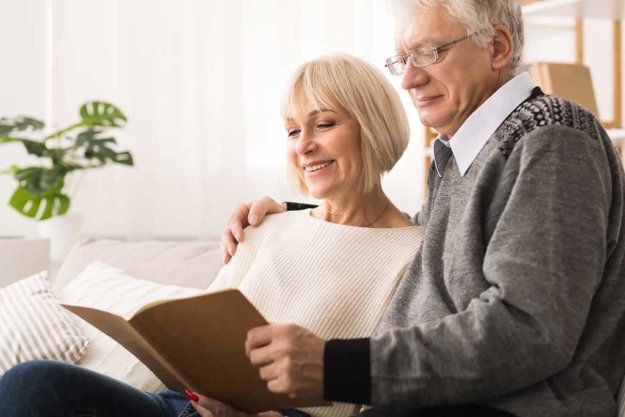 Happy elderly couple looking at photo album together Happy elderly couple looking at photo album together, having rest at home