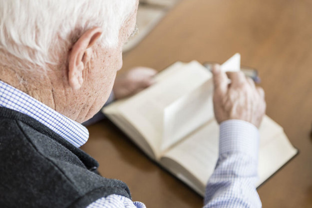 Senior man reading book relaxed at home, back view