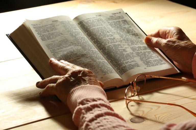 Hands of old woman with Bible on table and dark background 5 Spiritual Activities For Seniors With Alzheimer's Disease