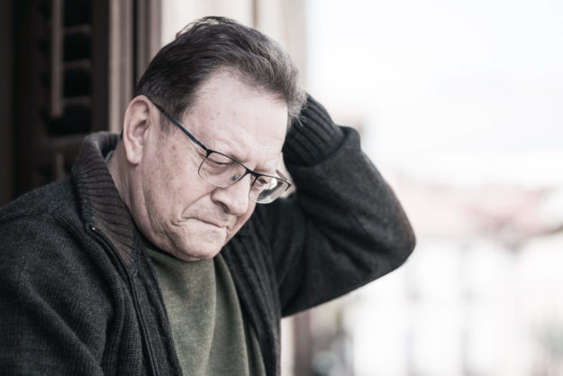 dramatic portrait of sad and depressed mature man 65 - 70 years old at home balcony lonely and confused facing getting old and retirement alone looking away