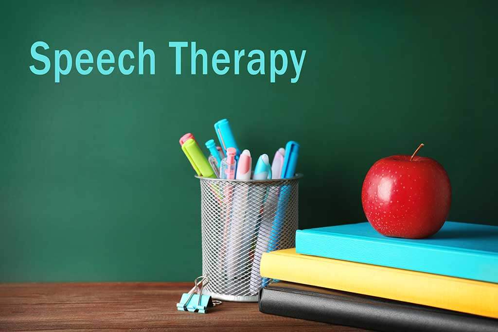 Colorful school stationery on table on blackboard background School stationery on wooden table. Text SPEECH THERAPY on chalkboard