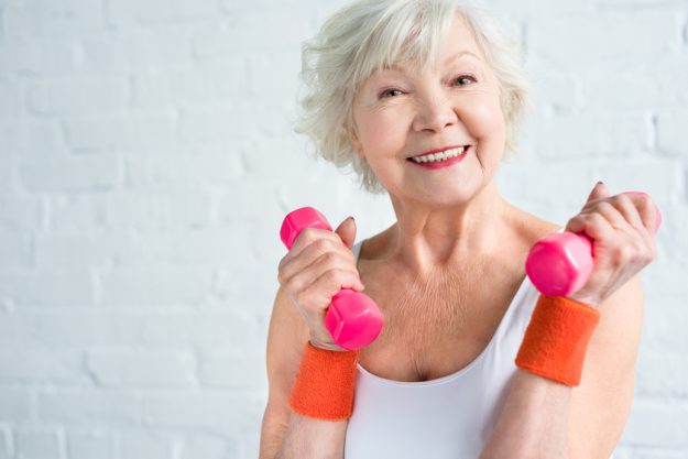 happy senior woman exercising with dumbbells and smiling at came Tips For Getting Fit For Women Over 50
