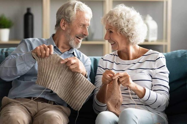 old husband and wife sit relax on couch in living room knitting together old husband and wife sit relax on couch in living room knitting together