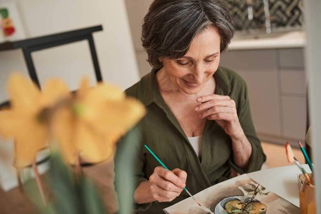 Woman sitting calmly at the table and drawing great picture with watercolors Woman sitting calmly at the table and drawing great picture with watercolors