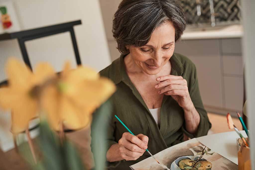 Woman sitting calmly at the table and drawing great picture with watercolors