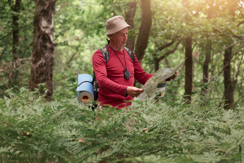 Image of traveler man searching right direction on map, like to travel along nature. Old tourist with backpack standing in amazing forest among trees. Active recreation and health lifestyle concept. Image of traveler man searching right direction on map, like to travel along nature. Old tourist with backpack standing in amazing forest among trees. Active recreation and health lifestyle concept.