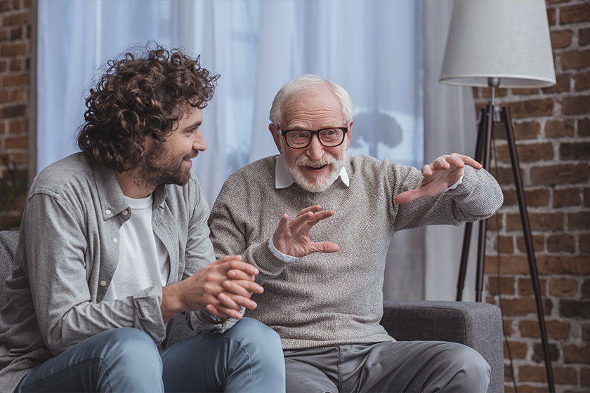 adult son and senior father talking on sofa at home