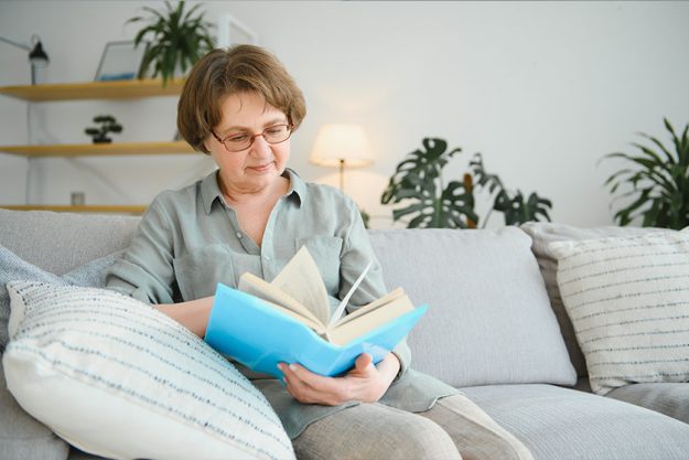 Old lady sitting on couch and enjoying interesting novel stock photo Old lady sitting on couch and enjoying interesting novel stock photo