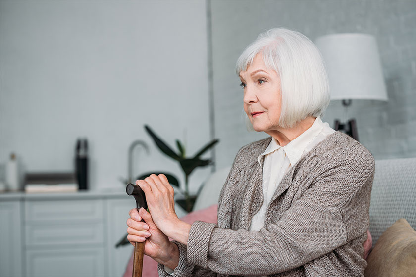 Side view of grey hair lady with wooden walking stick resting on couch at home