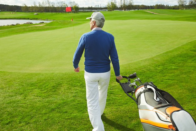 senior man walking down green field and carrying bag with bunch of golf clubs senior man walking down green field and carrying bag with bunch of golf clubs