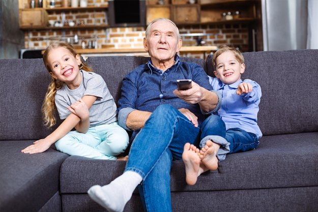Caring retired man watching TV with his grandchildren Caring retired man watching TV with his grandchildren