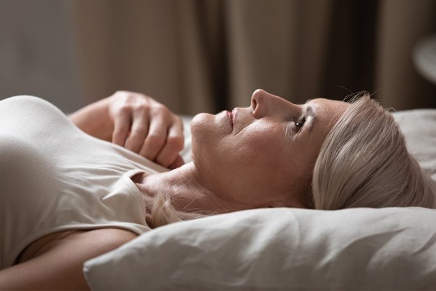 Disturbed mature older woman lying awake in uncomfortable bed