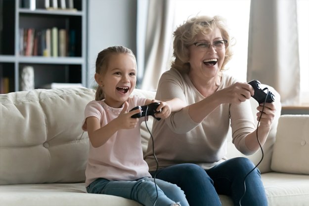 Excited laughing little granddaughter and grandmother wearing glasses playing video game together Excited laughing little granddaughter and grandmother wearing glasses playing video game together