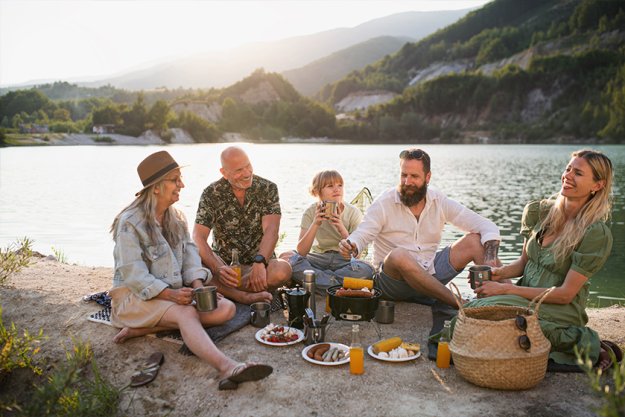Happy multigeneration family on summer holiday trip, barbecue by lake