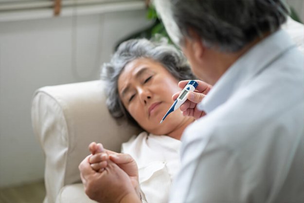 Sick Asian Senior Woman laying on couch while her husband holding and looking to temperature. Sick Asian Senior Woman laying on couch while her husband holding and looking to temperature.