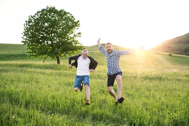 An adult hipster son and his senior father jumping in nature at sunset. An adult hipster son and his senior father jumping in nature at sunset.