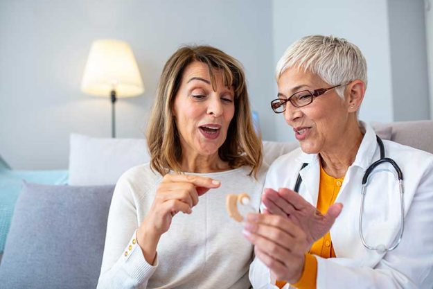 The doctor laryngologist explains senior woman how to wear a hearing aid The doctor laryngologist explains senior woman how to wear a hearing aid