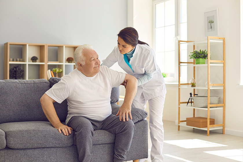 Nurse helping senior man to stand up from sofa