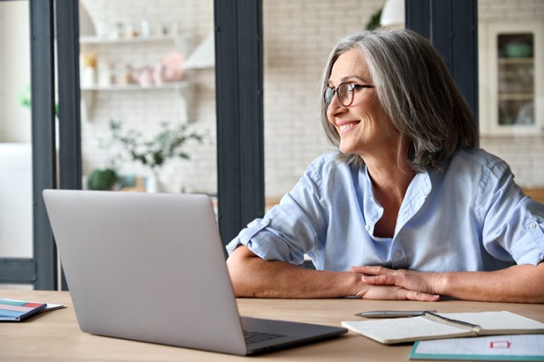 Middle aged woman sitting at home with computer smiling dreamingly. Middle aged woman sitting at home with computer smiling dreamingly.