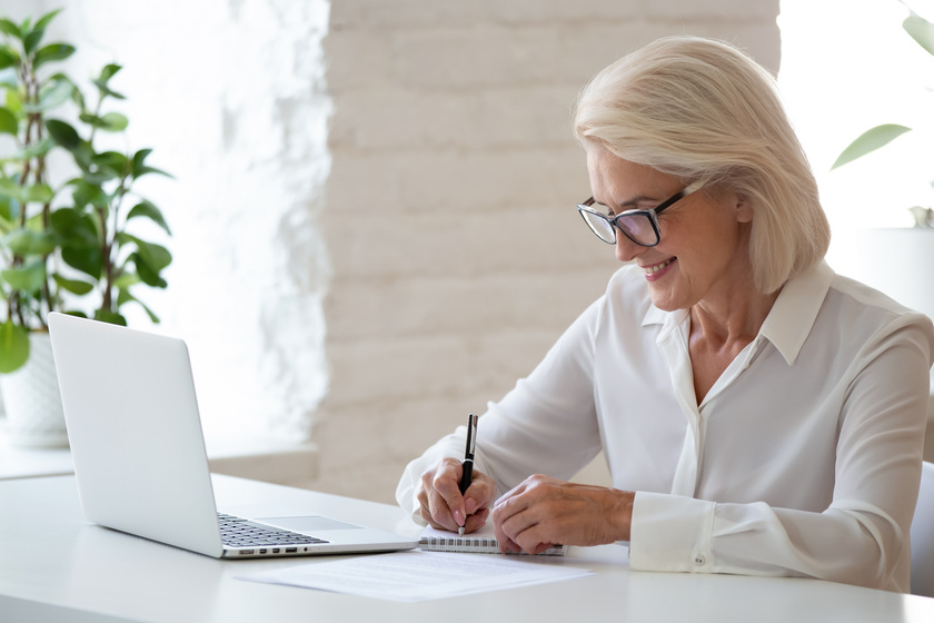 Mature businesswoman sitting at desk makes notes writing on notepad 5 Questions To Ask When Reviewing A Memory Care Community For Your Parent