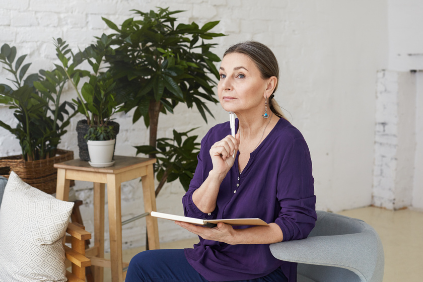 Picture of beautiful thoughtul mature 50 yeard old female writer in casual clothes sitting on comfortable chair in modern living room interior and making notes in copybook, having pensive look How Can Writing Be Beneficial In Your Golden Years?
