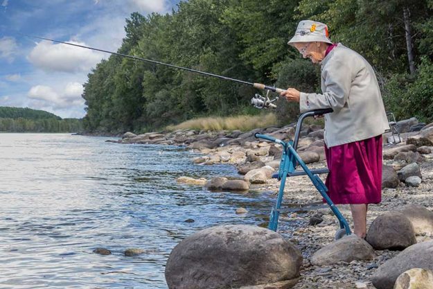 horizontal image of an elderly senior woman with a walker fishing at the edge of the lake horizontal image of an elderly senior woman with a walker fishing at the edge of the lake
