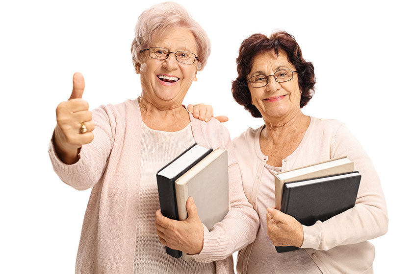 Cheerful elderly women with books making a thumb up gesture