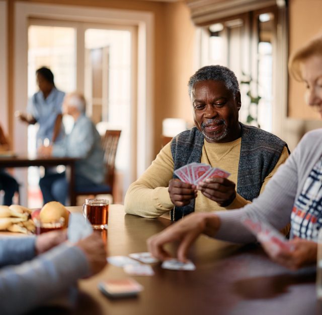 Happy black senior plays cards with friends in nursing home.