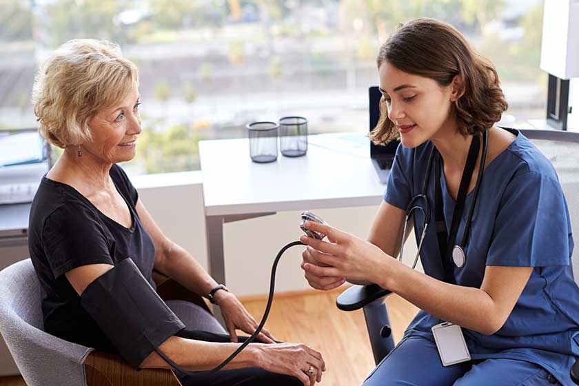 Nurse Wearing Scrubs In Office Checking Senior Femal Nurse Wearing Scrubs In Office Checking Senior Femal