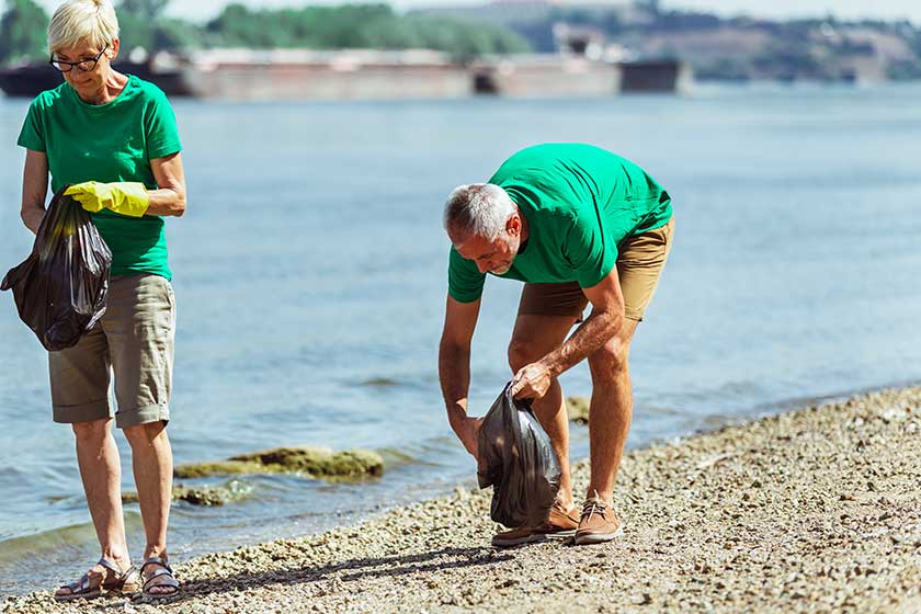 Senior volunteers gathering garbage on river bank Senior volunteers gathering garbage on river bank