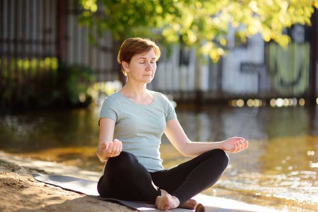 Mature woman practicing yoga outdoor exercise on the beach near the river. Mature woman practicing yoga outdoor exercise on the beach near the river.
