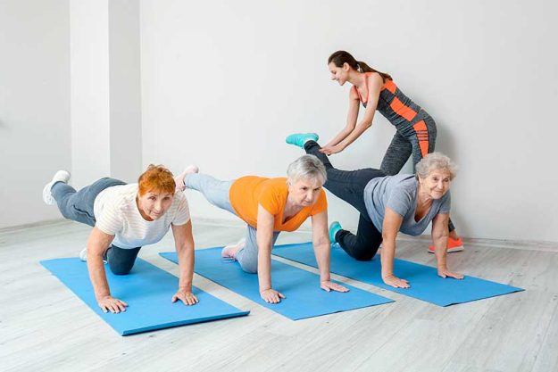 Young trainer helping elderly people during training in gym Young trainer helping elderly people during training in gym