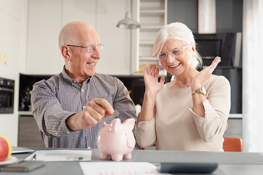 Senior couple putting coin into piggy bank
