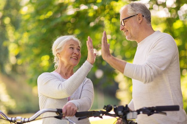Senior couple with bikes making high five at park
