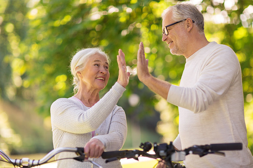 Senior couple with bikes making high five at park Senior couple with bikes making high five at park