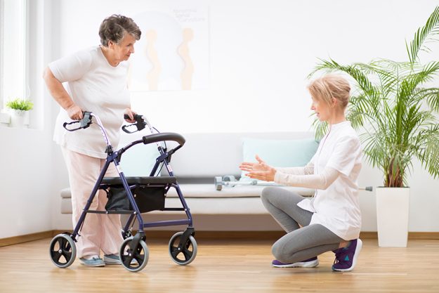 Senior woman with walker trying to walk again and helpful physiotherapist supporting her