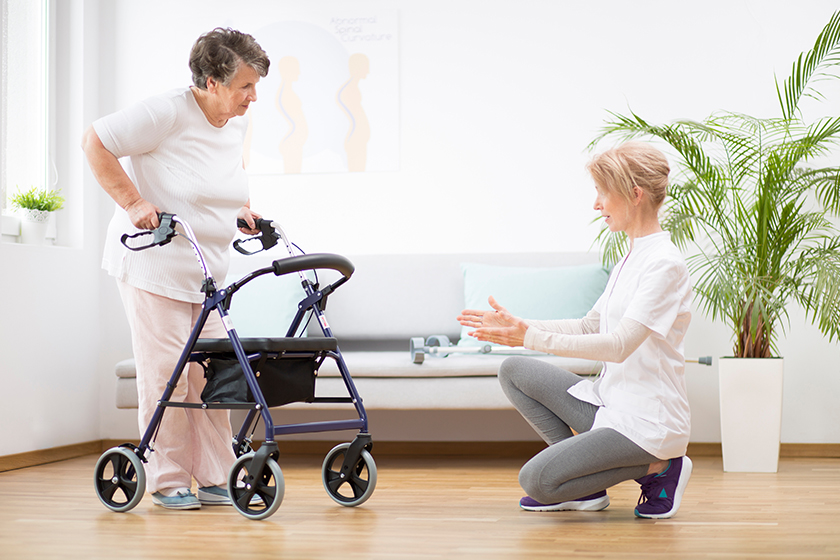 Senior woman with walker trying to walk again and helpful physiotherapist supporting her Senior woman with walker trying to walk again and helpful physiotherapist supporting her