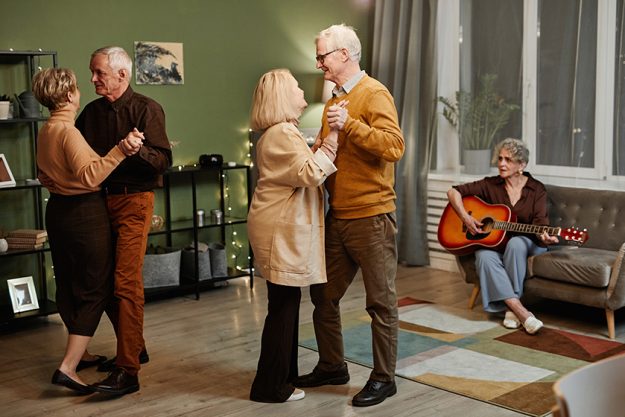 Two Caucasian senior couples dancing in decorated with lights living room