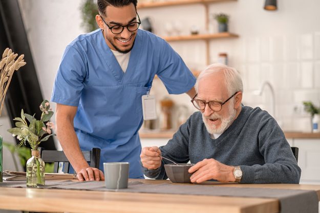 Joyous caregiver watching the pensioner eating breakfast Joyous caregiver watching the pensioner eating breakfast