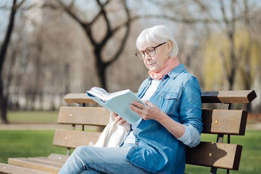 Retired woman reading a book on the bench Retired woman reading a book on the bench