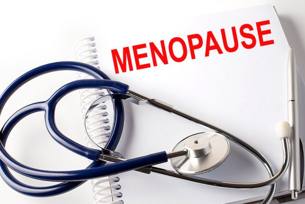 Stethoscope pen and hand text 'Menopause ' on notebook