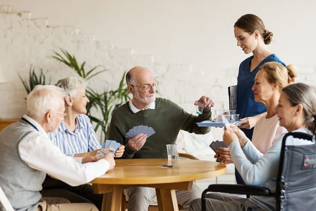 Young nurse bringing vitamin pills for senior man playing cards