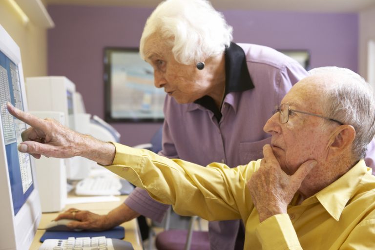Senior woman helping senior man use computer
