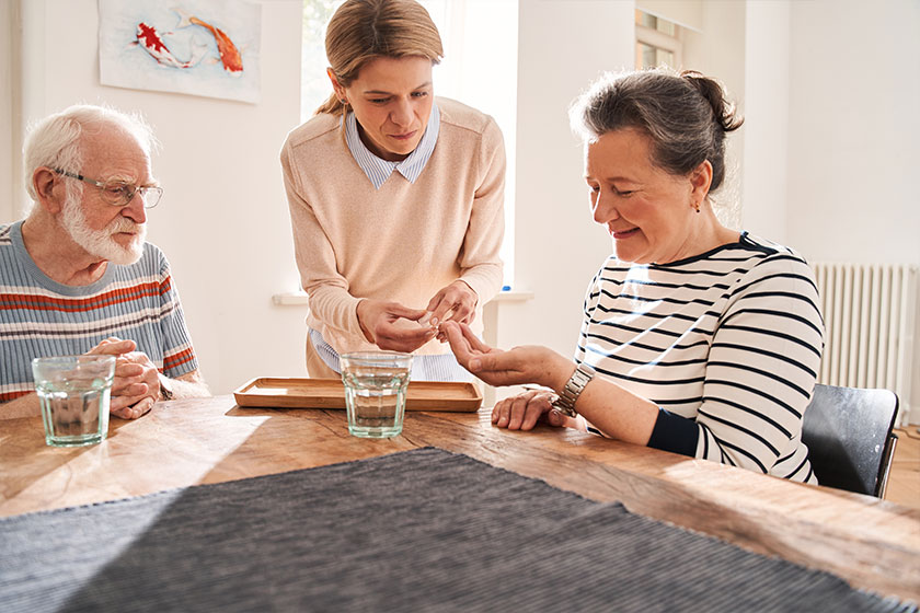 Nurse putting glass of water and pills in front of the two pensioners